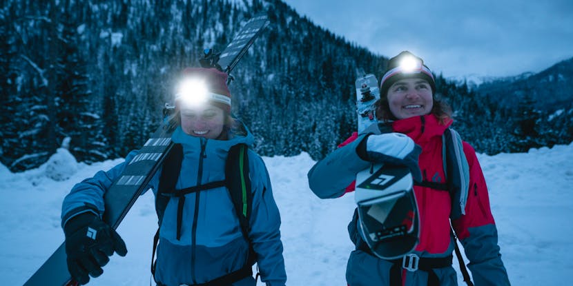 Two skiers in Black Diamond Recon Shells and smiles on their faces look up at their touring zone in the early morning light.