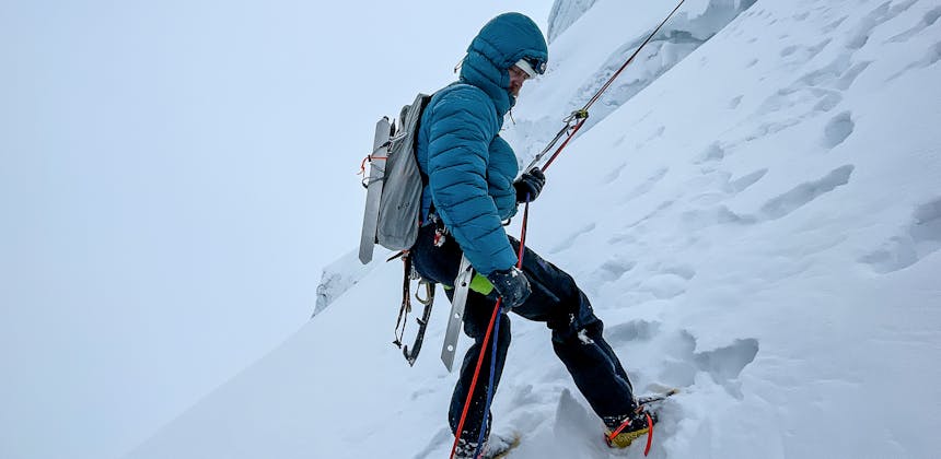 A mountaineer rappels from a snow anchor